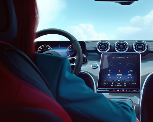Driver using the Mercedes-Benz MBUX infotainment touchscreen inside a luxury SUV.