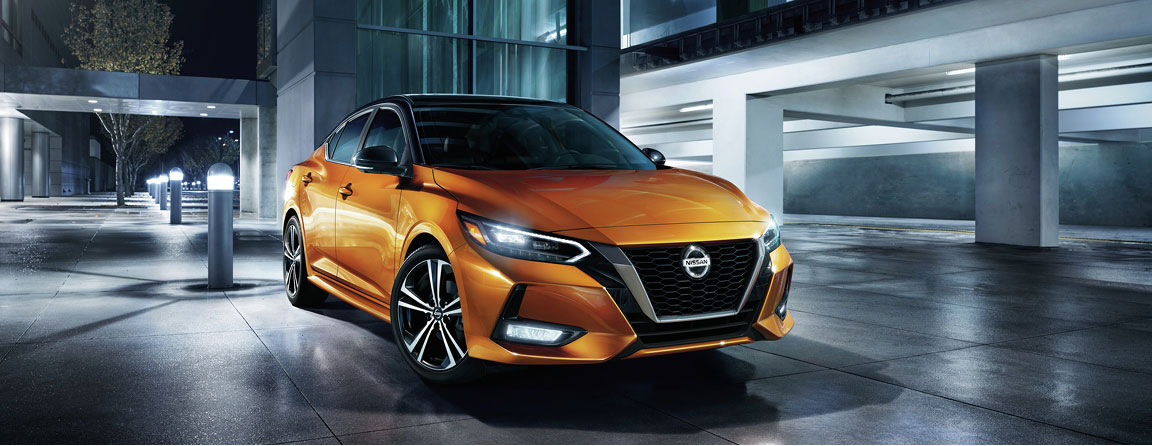 Orange Nissan Sentra sedan parked outside a modern building at night