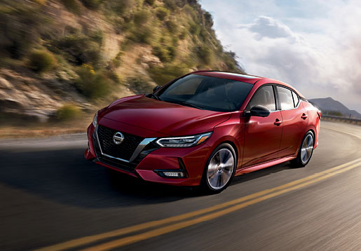 Red Nissan Sentra sedan driving on a scenic mountain road