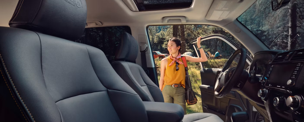 Toyota Tacoma interior with premium front seats and a person entering through the open driver's door at an outdoor recreation area.