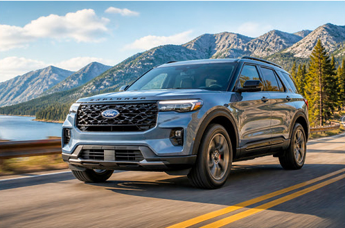 Blue Ford Explorer SUV driving along a mountain highway beside a lake showcasing family travel and road trip capability.