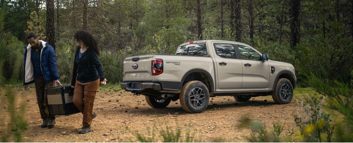 Ford Ranger truck parked in wooded area with couple unloading gear