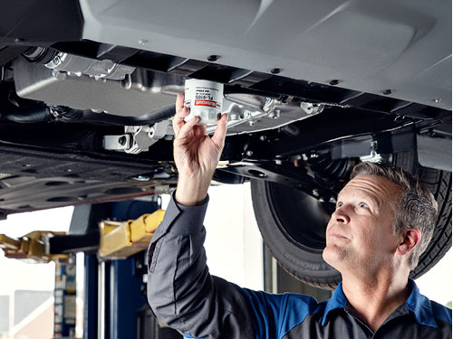 Ford technician installing a new oil filter under a raised vehicle on a service lift