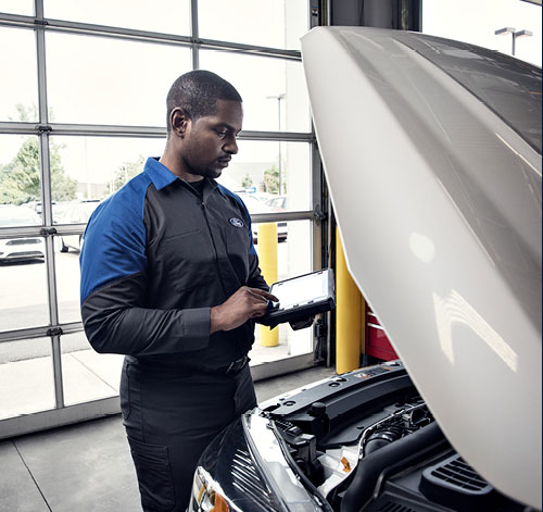 Ford service technician using a tablet to record a multi-point inspection at an open hood