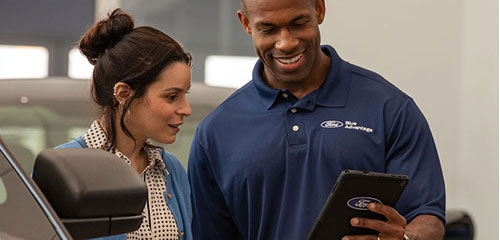 Ford service advisor reviewing vehicle information on a tablet with a customer in the showroom