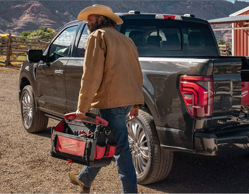 Man carrying a toolbox beside a Ford F-150 full-size pickup truck at a ranch