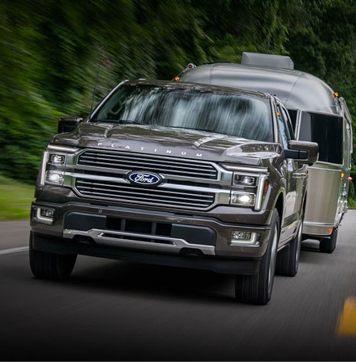 Ford F-150 Platinum full-size pickup truck towing a travel trailer on a tree-lined road