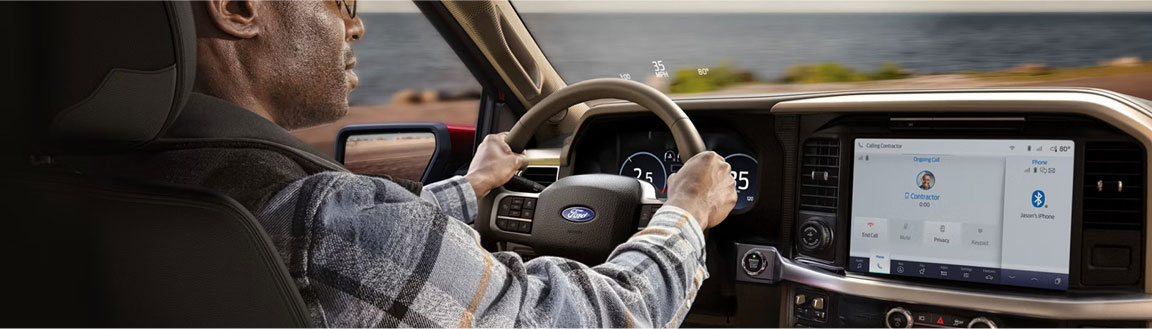 Driver using the Ford F-150 infotainment system while driving along a coastal road
