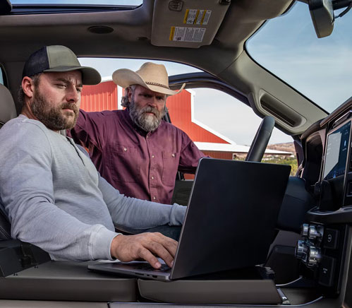 Two men using a laptop inside a Ford F-150 pickup truck at a ranch