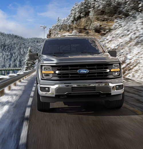 Ford F-150 full-size pickup truck driving on a snowy mountain road in winter conditions