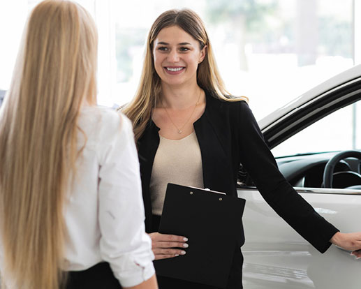 Dealership sales representative speaking with a customer beside a vehicle in a showroom