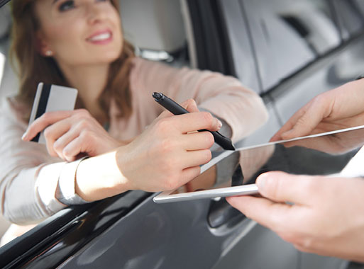 Customer signing vehicle purchase paperwork while holding a credit card at an auto dealership