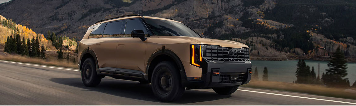 Kia Telluride three-row SUV driving on a mountain road beside a lake