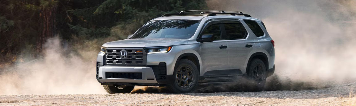 Honda Passport midsize SUV driving off-road on a gravel trail surrounded by forest