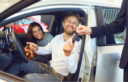 Couple receiving vehicle keys from a sales representative while sitting inside a car at a dealership