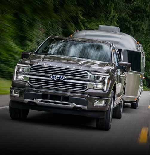 Ford F-150 Platinum full-size pickup truck towing a travel trailer on a tree-lined road