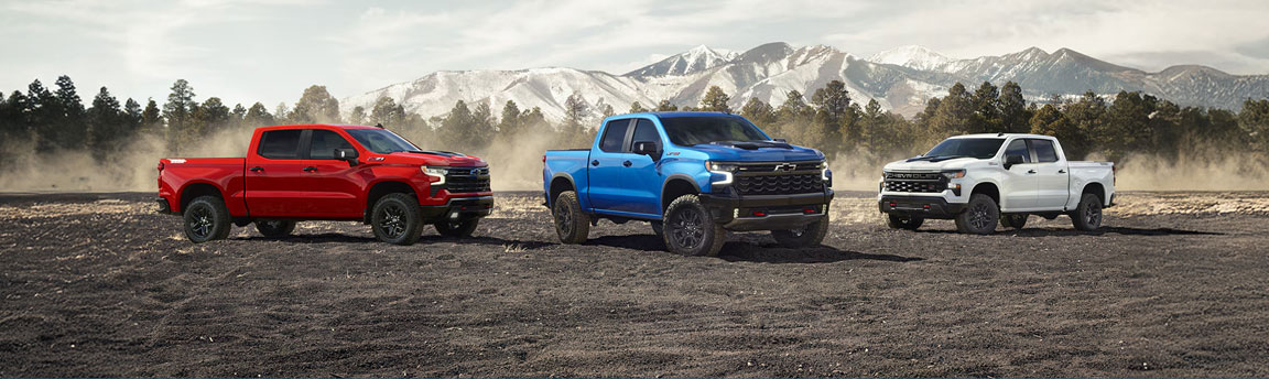 Three Chevrolet Silverado full-size pickup trucks displayed on rugged terrain with snow-covered mountains in the background