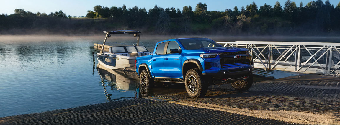 Blue Chevrolet Colorado truck towing boat at lake dock