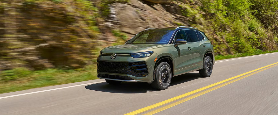 Green Volkswagen Tiguan driving on a scenic mountain road