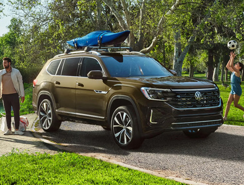 Volkswagen Atlas SUV with a roof-mounted kayak parked at a park while a family enjoys outdoor activities.