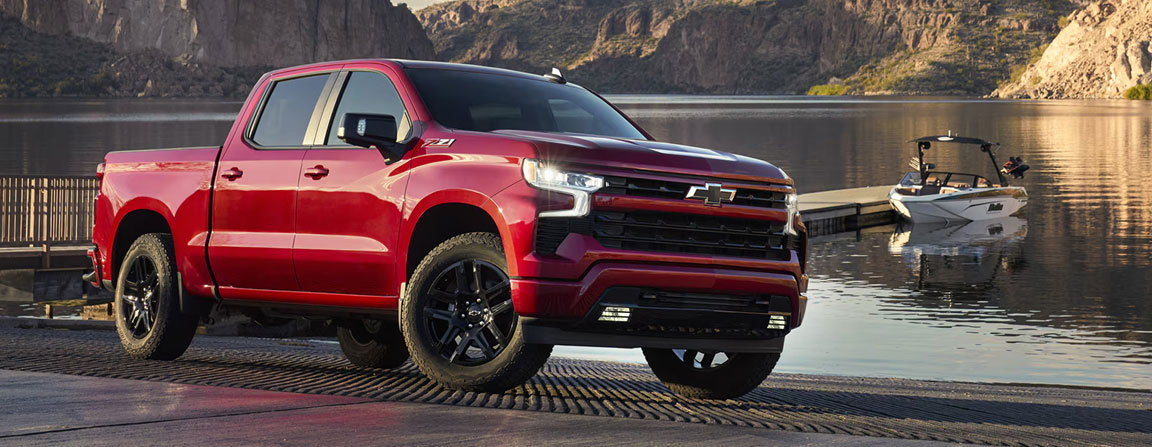 Red Chevrolet Silverado pickup truck parked by a lake with a boat