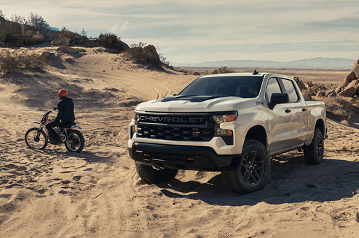 White Chevrolet Silverado pickup truck on a desert trail with dirt bike rider