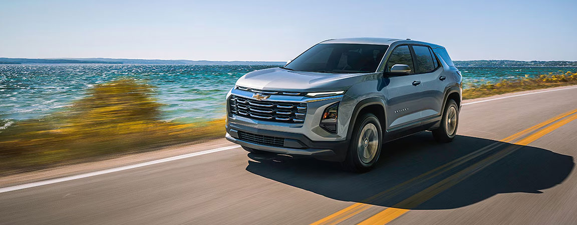 Silver Chevrolet Equinox driving along a scenic waterfront road